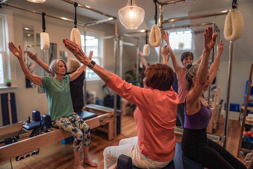A group reformer Pilates session reaching overhead at the towers